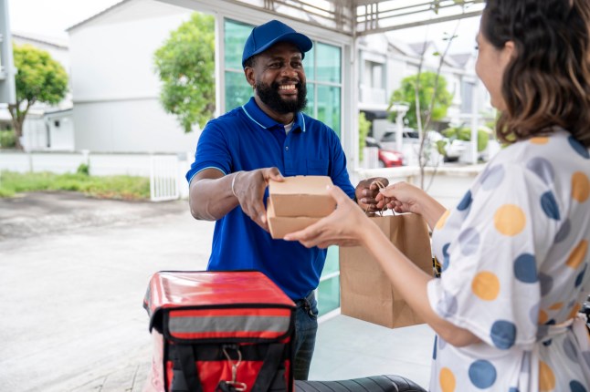 Smiling woman customer receiving home delivery take away food order from delivery man at home. Eating at home concept.