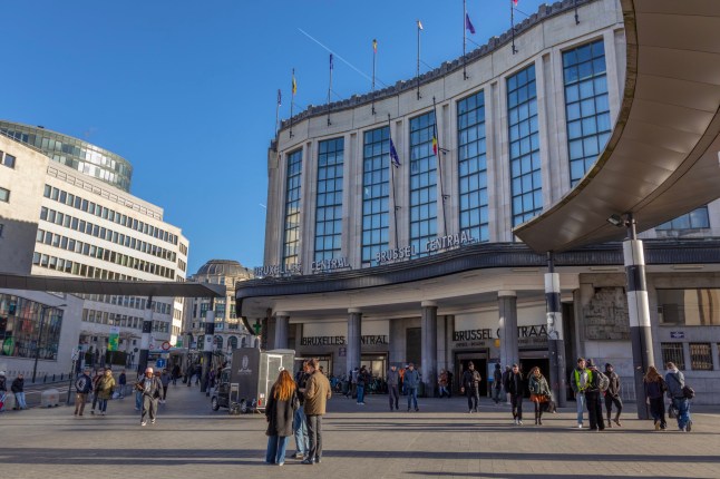 Brussels, Belgium ??? December 30, 2025: View of Brussels Central Station (Brussel???Centraal / Bruxelles???Central) in the city center. The curved stone fa??ade with tall vertical windows forms the main entrance to the station, part of the North???South rail connection completed in 1952 to designs by architect Victor Horta. In the foreground, pedestrians walk across the open plaza, with travelers entering and exiting the station through the main doors. Small groups stand talking near the entrance, while others cross the square or wait along the edges of the forecourt.