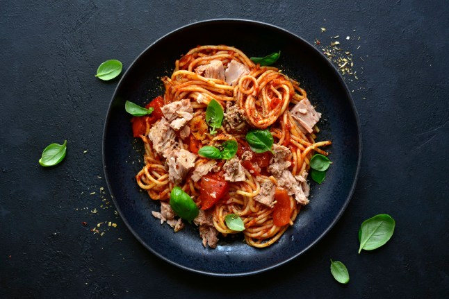 Pasta spaggeti with tuna and tomato sauce in a black bowl on a dark slate, stone or concrete background. Top view with copy space.